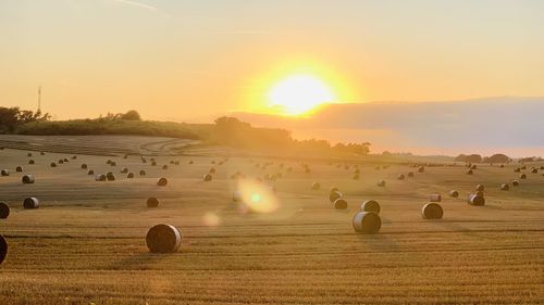 Hay bales on field against sky during sunset