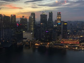 Illuminated buildings by river against sky in city