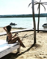 Woman sitting on beach by sea against sky
