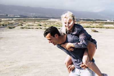 Young man giving piggyback to woman at beach