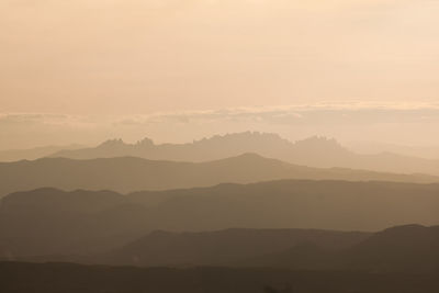 Scenic view of mountains in fog at dusk against cloudy sky