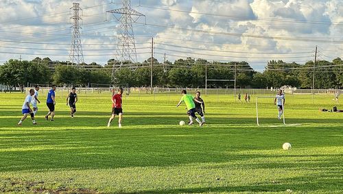 People playing soccer field against sky