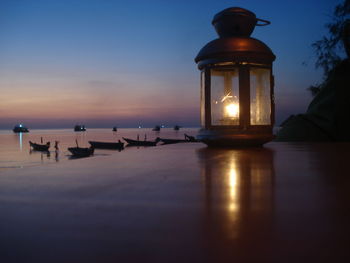 Illuminated lamp by sea against sky at sunset