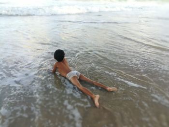 Rear view of carefree shirtless boy lying on shore at beach