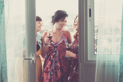 Smiling friends holding wineglasses seen through doorway