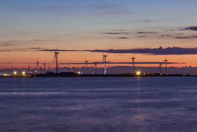 Illuminated traditional windmill by sea against sky during sunset