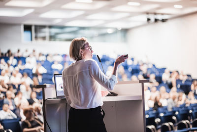 Female speaker giving a talk on corporate business conference. unrecognizable people in audience at