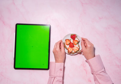Woman holding soft cheese and strawberry sandwich near green screen tablet