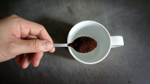 Hand holding spoon of coffee powder over cup