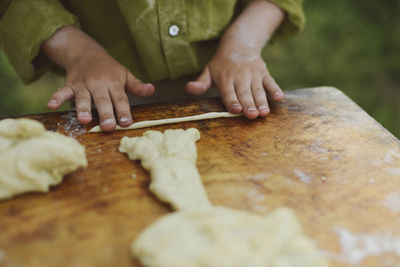 Midsection of boy preparing dough on wooden table at yard