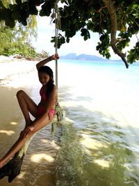 Portrait of smiling young woman sitting on beach against sky