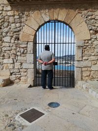 Rear view of man looking through closed gate