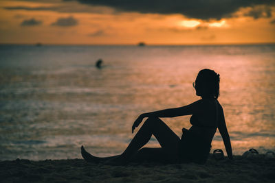 Rear view of silhouette man standing on beach against sky during sunset