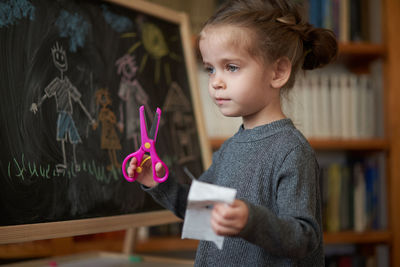 Girl holding paper and scissors in classroom