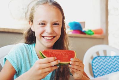 Close-up portrait of girl eating watermelon while sitting at home