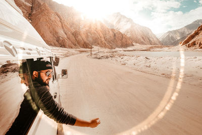 Man looking through car window on dirt road against mountains