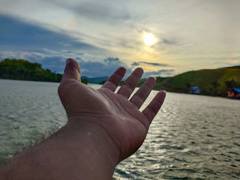 Midsection of person in sea against sky during sunset