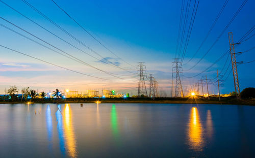 Electricity pylon by river against sky during dusk