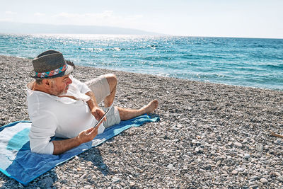 Middle-aged bearded man resting on beach and reading ebook on electronic tablet. concept of reading