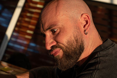 Close-up of a man with a shaved head and a black beard with a crazy expression.