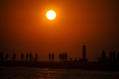 Silhouette people by sea against sky during sunset