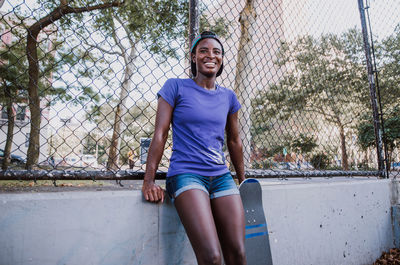 Portrait of smiling young woman standing against fence