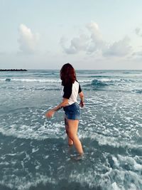 Rear view of boy standing on beach against sky