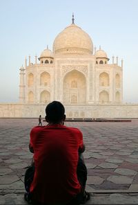 Rear view of man sitting against taj mahal