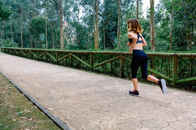 Full length of woman running on footpath against trees