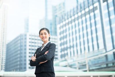 Portrait of businesswoman with arms crossed standing against buildings in city