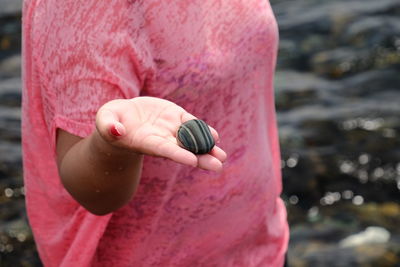 Midsection of woman holding pebble at shore