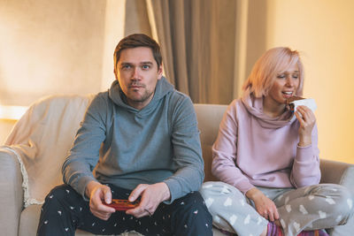 Young family in home clothes playing video games on couch in living room