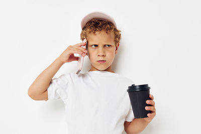 Boy talking on phone while holding coffee cup against white background