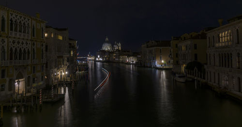 Canal amidst illuminated buildings at night