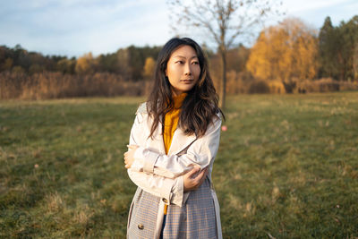 Middle aged asian woman in coat looking away walking in autumn forest