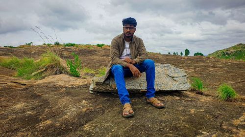 Man sitting on rock against sky