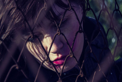 Close-up of thoughtful young woman with messy lipstick by fence