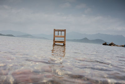 Abandoned chair in lake against sky