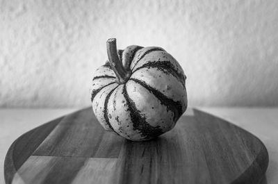 A single mini green and white decorative pumpkin displayed on a wooden chopping board monochrome