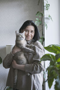 A young woman holds a gray cat with yellow eyes in her arms. the cat and her mistress at home. 