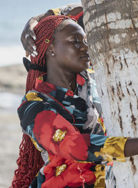 African woman hugging a palm tree that provides shade by a beach in accra ghana