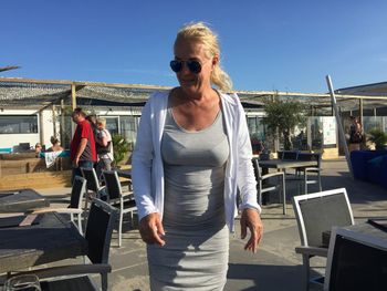 Fashionable mature woman in sunglasses standing at restaurant against sky