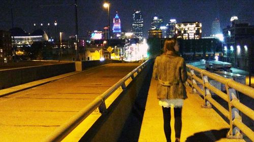 Rear view of woman walking on illuminated street at night