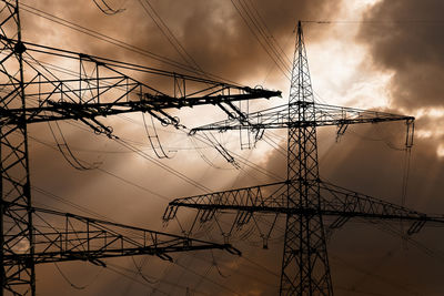 Low angle view of electricity pylon against cloudy sky