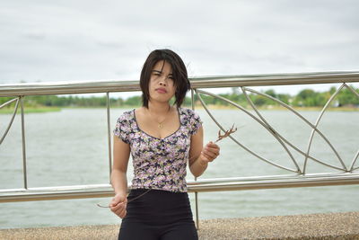 Portrait of young woman with short hair standing by railing against lake 