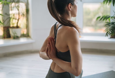 Young fit woman practice yoga doing asana in light yoga studio with green house plant