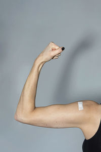 Woman with bandage flexing muscle over gray background