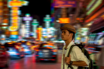 Side view of man with backpack walking in illuminated city at night