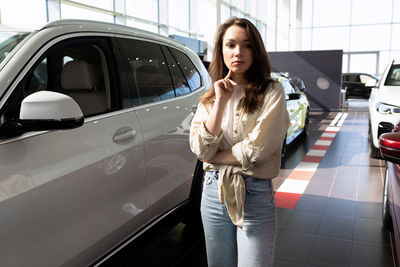 Portrait of young woman standing by car