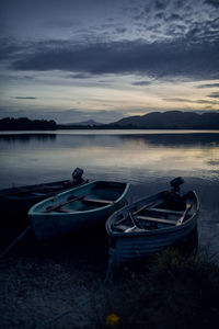 Boats moored in lake against sky at sunset